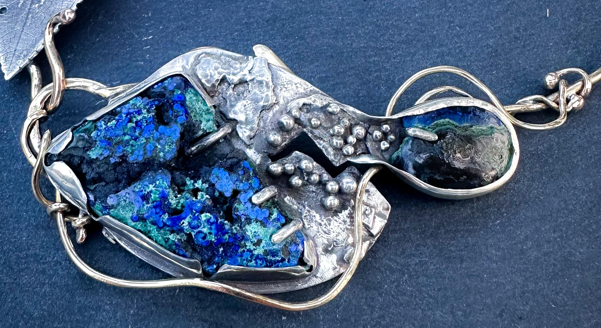 A close view of the small oval stone, the granulated metal bridge and the larger blue-green druse.